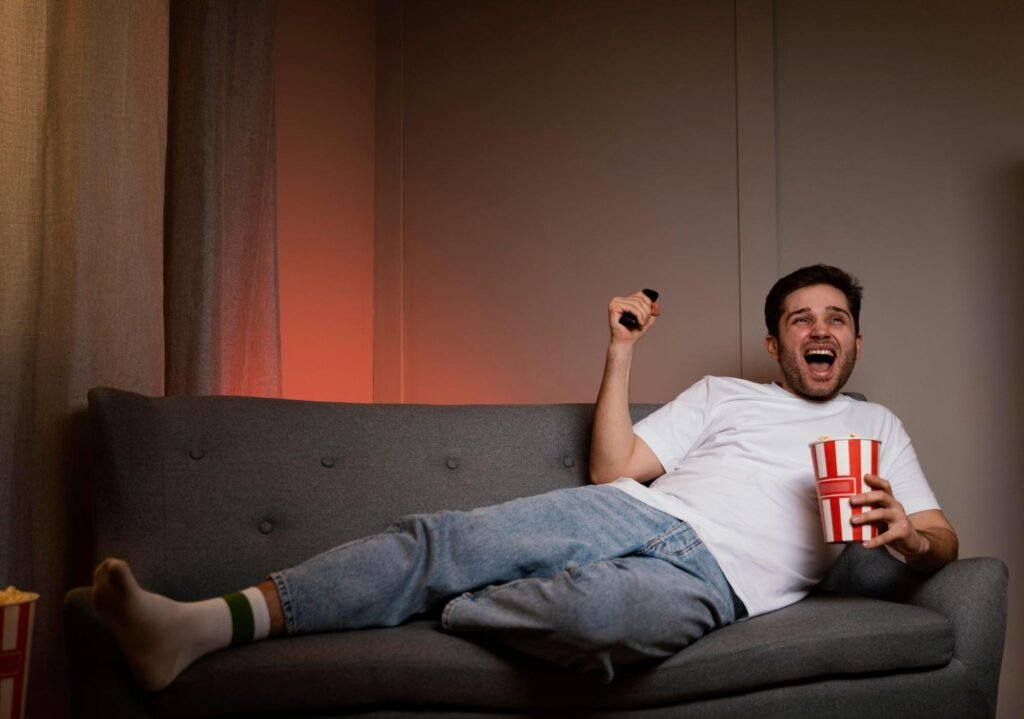 Man laughing while watching TV with popcorn on a couch